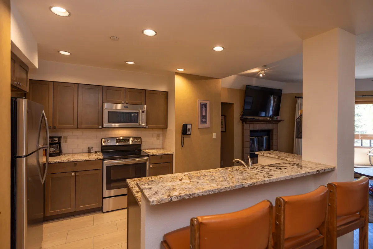A welcoming, modern kitchen featuring a granite countertop, stainless steel appliances, and bar stools. The open layout is ideal for cooking, entertaining, and gathering with loved ones, with plenty of workspace and a view from the kitchen area.
