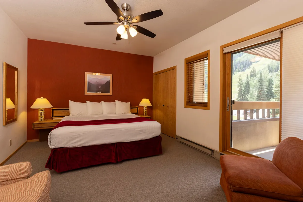 This image features a tranquil primary bedroom with a king-sized bed dressed in plush bedding, a cozy armchair stationed near a window, and elegant nightstands. Soft natural light filters in, creating a calm and restful ambiance ideal for relaxation after an adventurous day. The setting is styled to evoke comfort and the serene feeling of a mountain retreat.