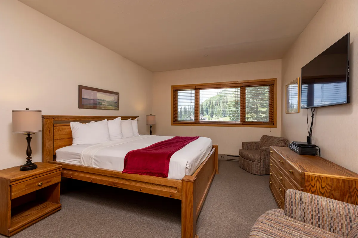 Here we see a secondary bedroom with a neatly made bed, window with natural light, an inviting armchair, TV, and dresser. The cozy setup and decorative touches make it ideal for families or groups, offering a welcoming retreat to unwind and recharge.