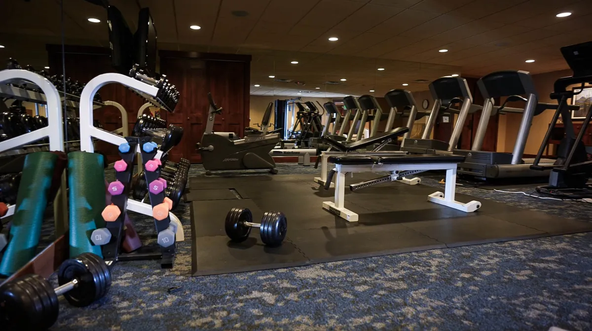 A bright, modern fitness center stocked with treadmills, weights, and various exercise machines, offering ample space for both strength training and cardio workouts. The energetic atmosphere suggests convenience and an active lifestyle.