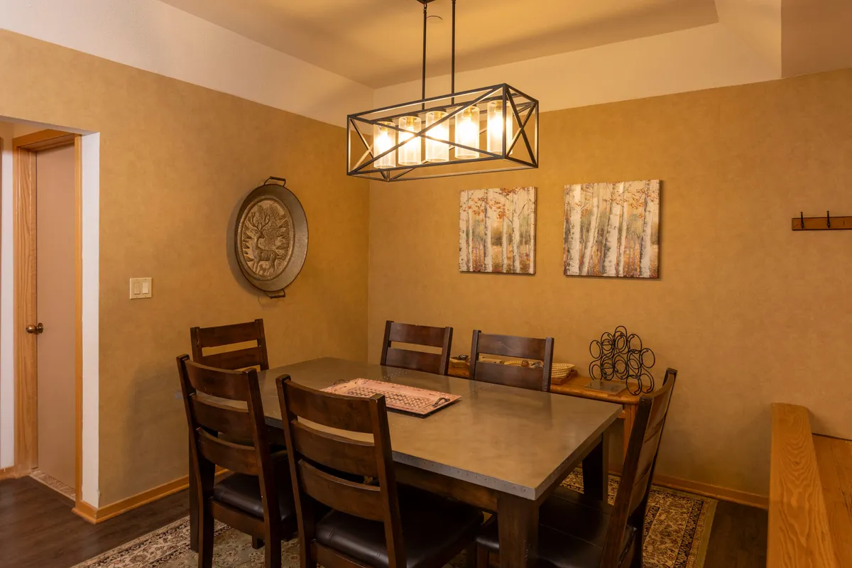 A cozy dining area featuring a large dining table beneath a chandelier, accented by wall art and a mirror. The setting invites group meals, board games, or sharing stories at the end of an adventure-filled day.