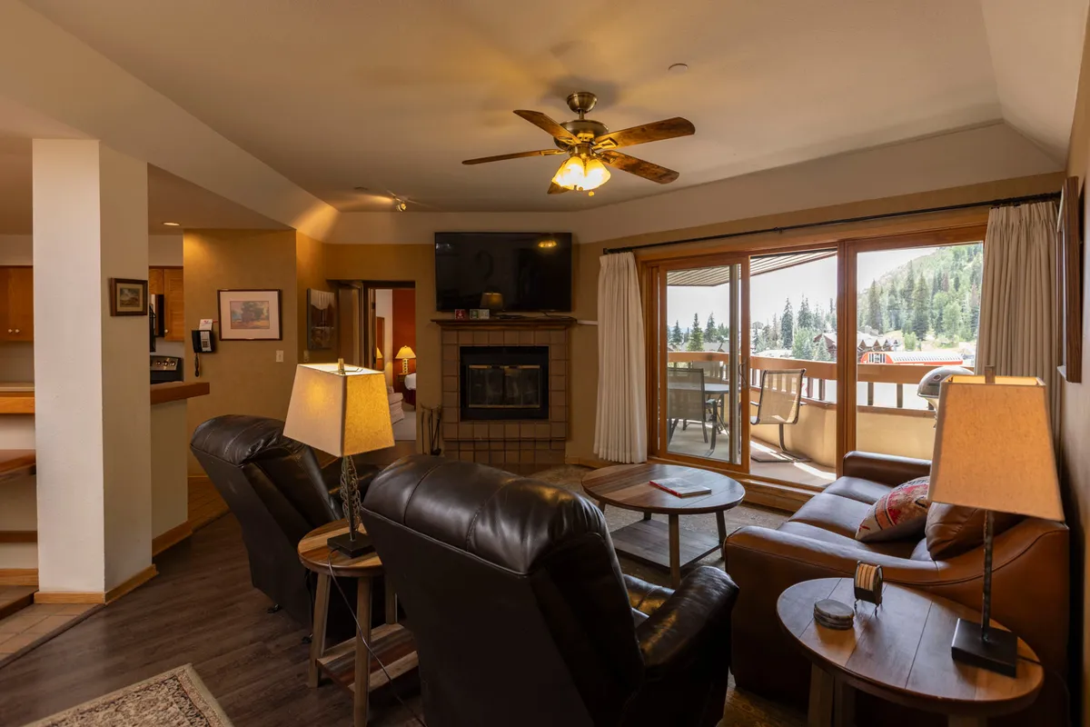 Another angle of the living area, highlighting the fireplace, large windows, and comfortable seating. The arrangement shows a welcoming space adorned with a decorative rug, inviting guests to relax, socialize, or simply admire the sunrise over the mountains.